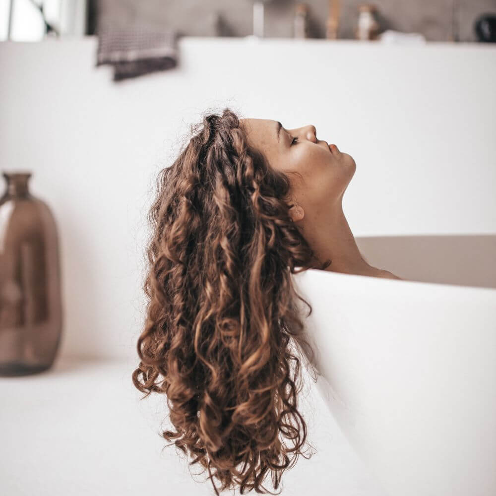 woman with long dark curly hair hanging over side of tub