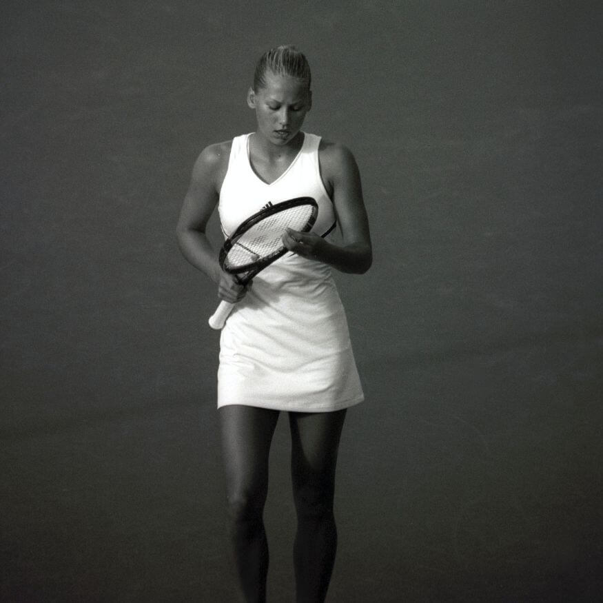 women in white outfit looking at tennis racquet