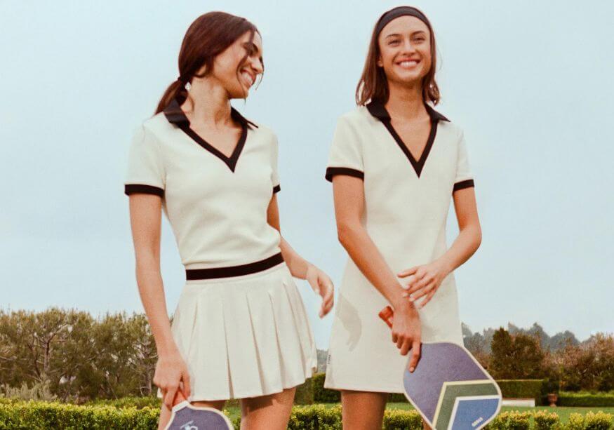 two girls in white pickleball outfits holding paddles