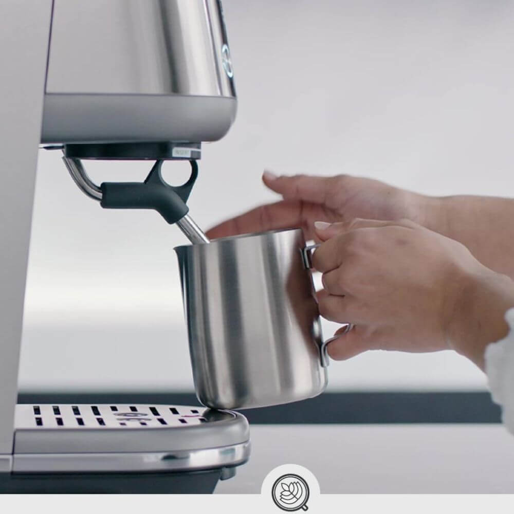 womans hands holding stainless steel milk frothing pitcher