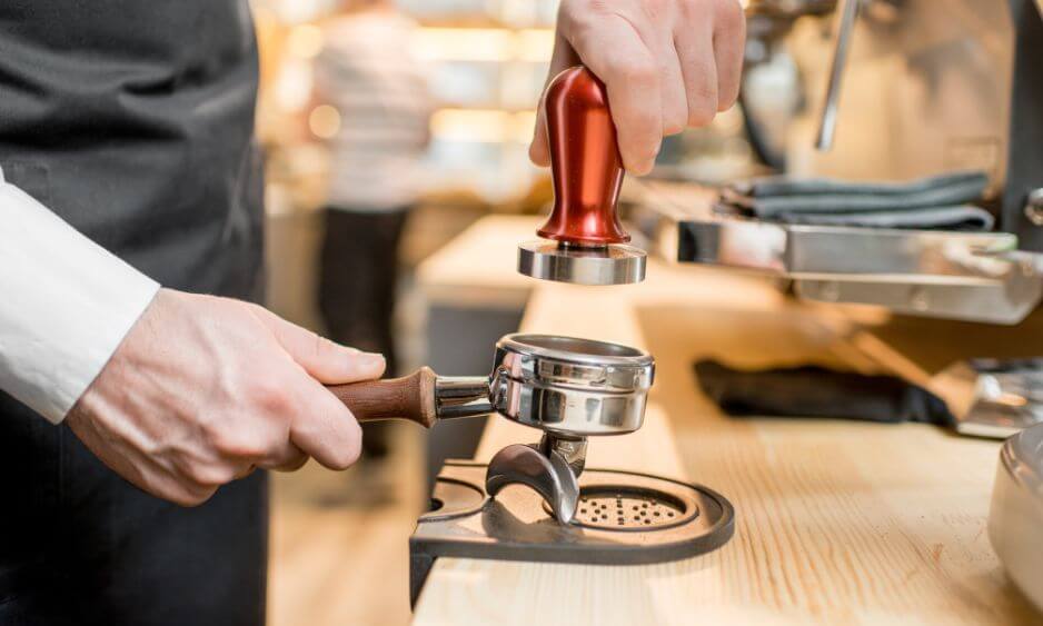 man with red handle tamper compacting espresso grounds