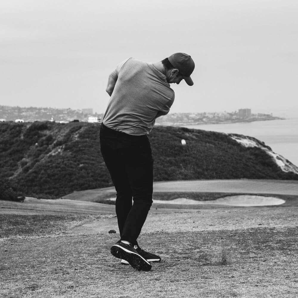 black and white image of golfer hitting a golf ball overlooking ocean